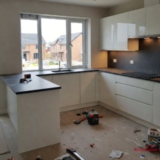 белая глянцевая с-образная кухня с черной столешницей